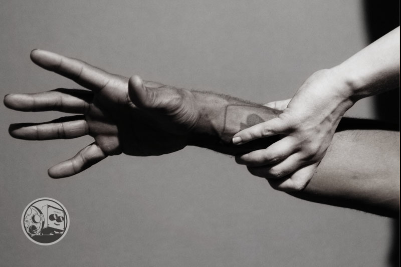 two hands, one reaching out to the left as the other grips their wrist.