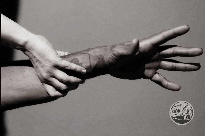 two hands, one reaching out to the right as the other grips their wrist.